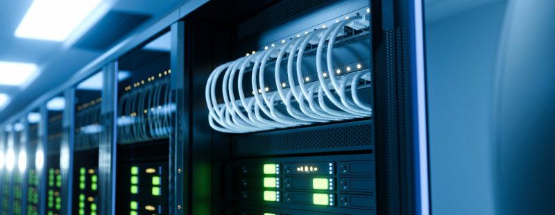 Close up of server rack cabinets with looped white ethernet cables and glowing green indicators in a professional data center, ideal for technology and cloud computing concepts.