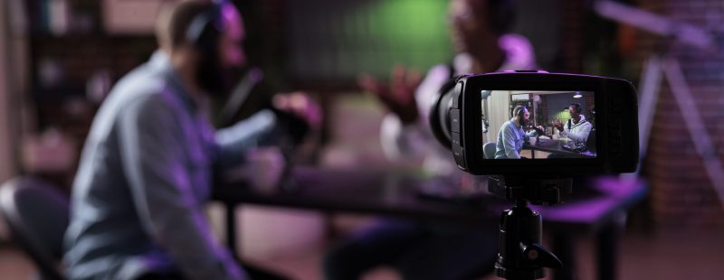 Multiethnic team of people meeting to broadcast internet podcast, recording video discussion on camera. Influencer and guest talking on online livestream to create social media channel content.